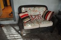 Front view of dark wicker outdoor love seat with floral cushions and three accent pillows.