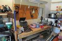 Workbench with bench grinder on right side, red vise attached to bench, assorted tools on table and hanging on pegboard, various equipment and hardware storage units