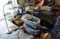 Table showing seven radios, silver floor lamp, plastic containers filled with stainless flatware and various painter's tapes and other small items.