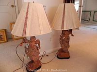 Full view of two matching carved wood lamps with oblong pleated shades positioned on carpet.