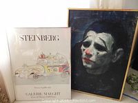 Photo of the clown head oil painting and Steinberg poster side by side, showing overall condition and framing.