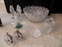 Several glass and crystal items including large crystal bowl, salt and pepper shakers, small lidded containers, and swan salt cellars on carpeted floor.