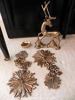 Brass stag figurine seated near chained brass starburst decorations and a brass sweetmeat dish on carpeted floor.