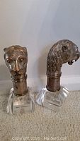 Both lion head sculptures on lucite bases side by side