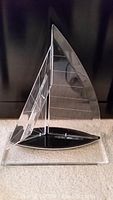 Front view of vintage Lucite sailboat showing clear pointed sails and black base with attachment points.