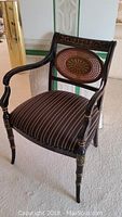 Full view of the black lacquered wooden armchair with oval caned back and striped padded seat.
