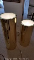 Front view of two gold-tone cylindrical stands with frosted tops on carpet