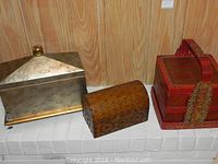 Photo showing the three boxes side by side: silver-tone metal box with embossed dome lid, studded domed wooden box, and red painted wooden box with tray and ornate basket handle.