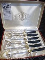 Six steak knives displayed inside an open satin-lined box with "The Connoisseur's Choice" emblem visible on lid interior