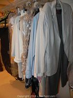Overview photo of hanging women's clothing including blazers, shirts, and pants, mostly in light tones and pastel shades