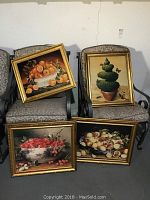 Four framed wall art pieces depicting fruit bowls and a nature scene displayed on chairs with patterned upholstery. Gold finished frames, show some wear.