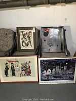 Four pieces of framed wall art displayed on chairs and floor in storage area, showing overall lot contents and size range