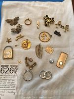 Assortment of jewelry pieces laid on cloth: brooches, pendants, earrings, caps, watch and clips
