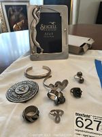 Displays the entire lot with rings, pins, bracelet, and pewter photo frame laid out on cloth.