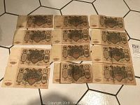 Twelve 1910 Russian 100 roubles banknotes laid out on tiled floor, showing front side with clear year 1910 and denomination 100