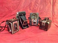 All four vintage cameras grouped on red fabric background showing overall condition and different models