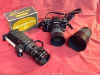 Yashica FX-103 camera body with bellows unit, Sigma zoom lens, and additional lens laid on a red cloth. Original bellows unit box placed behind items.