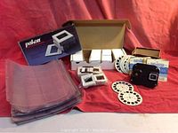 Full arrangement shot showing View Master viewer, boxed slide mounts, circular slides, and plastic storage sheets on a red cloth.