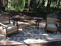 Two wood and cane back armchairs placed on an outdoor carpet with a long wooden table featuring a cane bottom shelf between them.