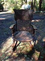 Front view of a dark wooden antique rocking chair with spindled back and carved armrests, showing wear and age.