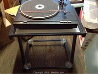 LXI series black turntable without top, positioned on a frosted glass and metal stand on wheels.