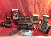 Full assortment of electronics including Bentley portable TV, Cobra walkie-talkies, LifeProof iPhone case, computer speakers, headphones, phone charger, landline phone, and flip phone.