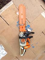 Full view of STIHL MS 260 chainsaw lying on cardboard, showing orange protective blade cover and body with visible wear.