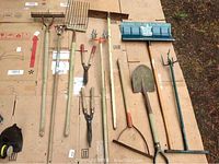 Top-down view showing all eleven yard tools arranged on cardboard outdoors.