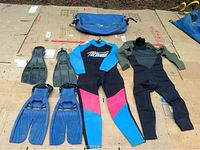Two wetsuits (medium and large), two sets of flippers (black short blades and blue long blades), and one blue carrying bag arranged on cardboard.