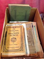 Box of vintage sheet music and music books with worn covers, includes The Golden Book of Favorite Songs in front.