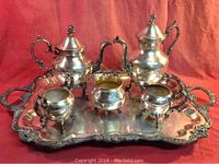 Full view of silver plated 6 piece tea service on tray showing heavy-duty silver plated teapot, coffee pot, creamer, sugar bowl (missing lid), waste bowl and ornate tray with floral designs.