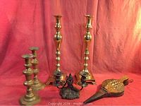 Overall view of the six items including two tall polished brass candlesticks, two smaller unpolished brass candlesticks, ornate double candlestick, and fire bellows.