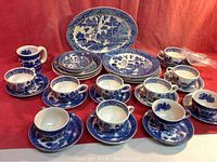 Full set including plates, bowls, cups with saucers, mug, napkin rings, and oval platter arranged on red backdrop.
