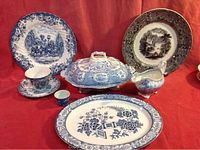 Photo showing various old china pieces including plates, serving dishes, gravy boat, and cup/saucer with blue and white floral and scenic patterns.