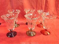 Photo of six clear glass parfait glasses with vertical ribbed design and colored bases in blue, green, and pink on an orange background.