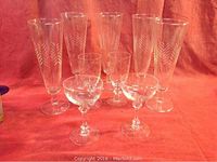 Five tall etched crystal pilsner glasses, two etched crystal sherry glasses, and two etched crystal port glasses arranged on cloth.