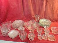 Wide view of assortment of mid-century textured clear glass bowls, trays, dishes, and cups on red background.