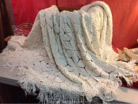 Large white crocheted tablecloth or bedspread draped over table showing leaf pattern and fringed edges