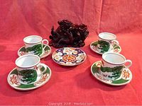 Four dragon-themed cups and matching saucers with a small decorative plate in the center, arranged on a red fabric.