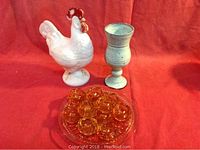 Front view of milk glass rooster candy dish, ceramic goblet, rose depression glass plate with amber bowls arranged on it.