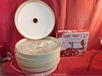 White food dehydrator with multiple trays stacked and Apple-Mate box behind it