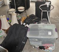 Overview of two black suitcases, plastic tote of clothing and steamer in garage