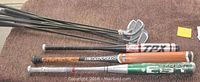 Several golf clubs and baseball bats on carpet, showing Easton baseball bat and two other bats with worn paint