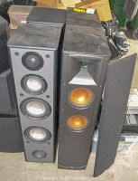 Front view of two pairs of floorstanding speakers side by side showing driver cones and grilles