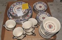 Top down image of all china pieces arranged in cardboard box showing different plates, bowls, cups and saucers with colorful floral and scroll patterns.