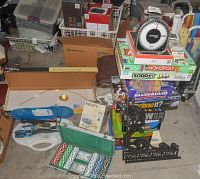 Photo shows the overall lot revealing poker chips set, boxed board games stacked, DYMO postal scale on top, hand tools, picture light box, and Krups steamer box.