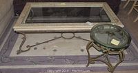Rectangular coffee table with crackled white wood frame and glass top, round custom end table with green tinted glass, and rug underneath showing parts of the design.