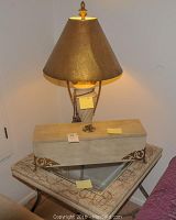 Photo showing the lamp with gold brown shade on top of the decorative cream and brown storage box, both sitting on the crackled cream side table with glass inset.