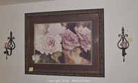 Framed floral artwork with roses and two metal wall sconces on either side