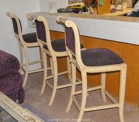 Three wooden barstools lined up next to a counter, showing the full height and detailed construction.
